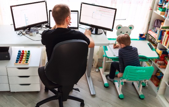 Person working on computer with a child drawing next to them