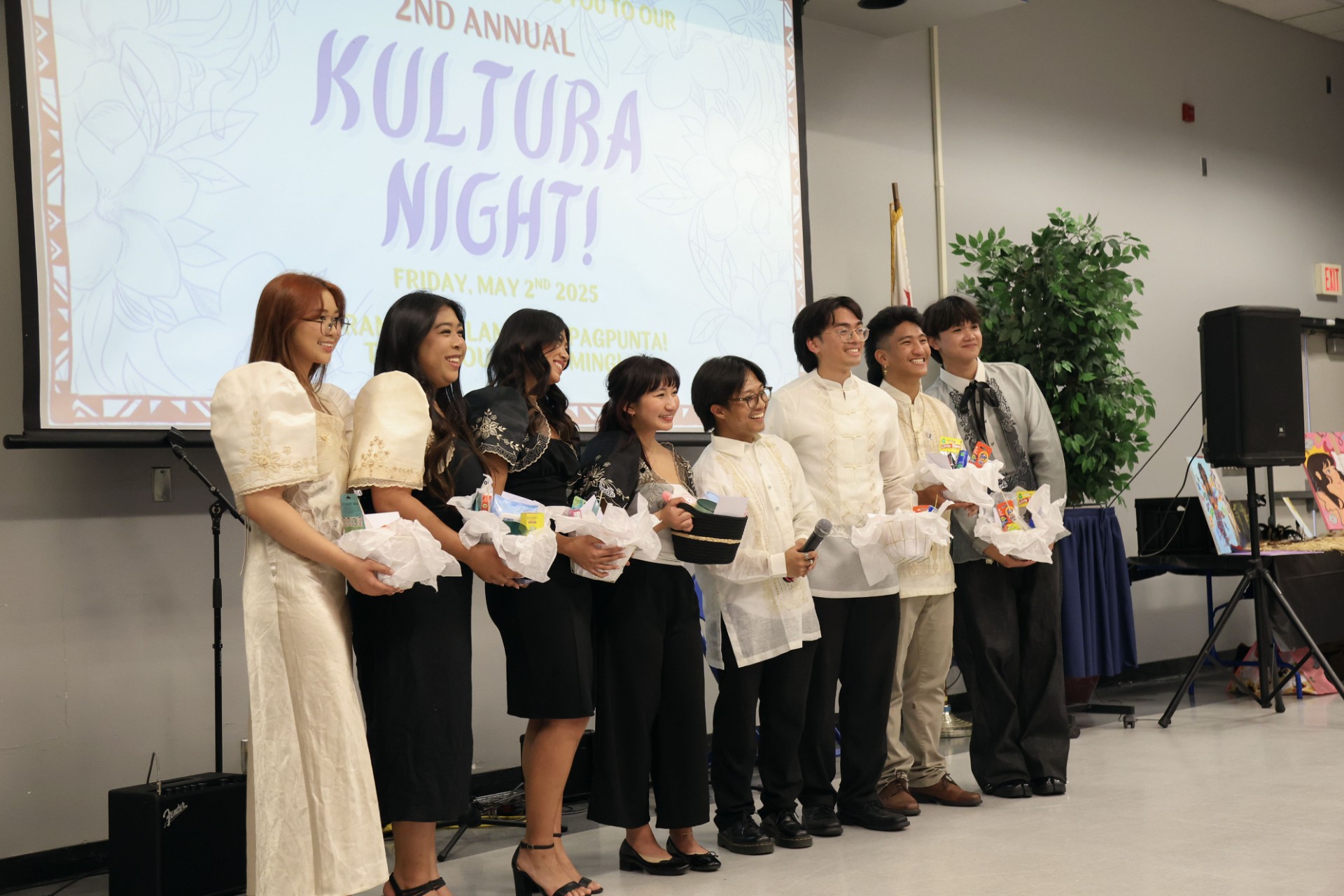 CSU Bakersfield Filipino Organization Kaibigan Kultura (Culture) Night Spring 2025 - Women in white filipinana (traditional Filipino clothing) and black filipinana are lined up with men in barongs (traditional Filipino clothing) in front of a sign that says "2nd Annual Kultura Night!"