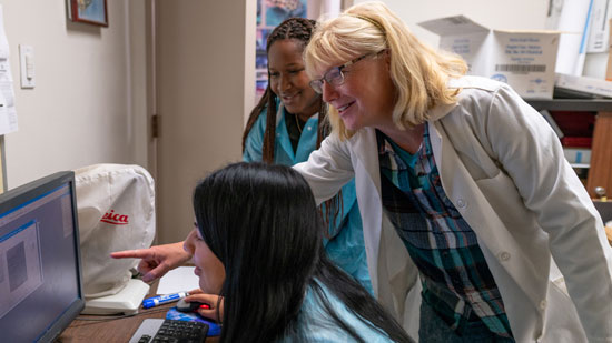 Nursing student on desktop computer with instructor leaning over her shoulder and pointing at screen