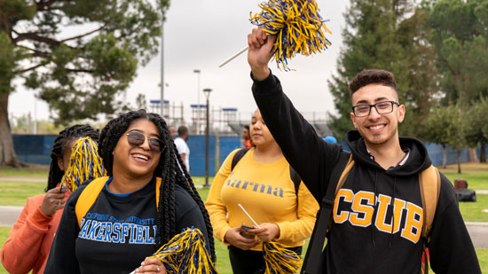 Two CSUB students smiling and holding pom-poms