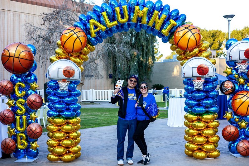 Alumni pose under a blue and gold arch at the 2024 Alumni Family Weekend