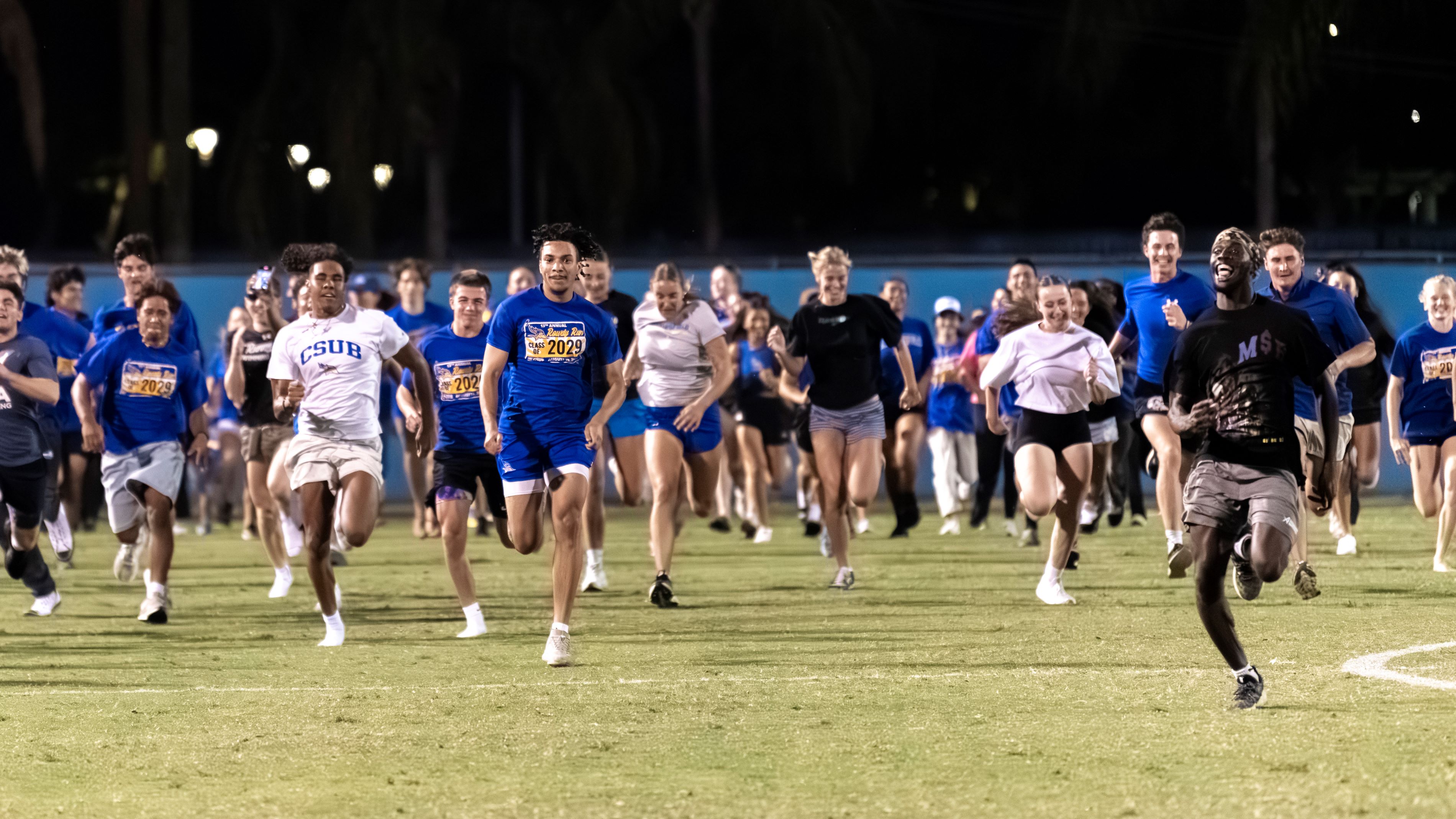 Group of CSUB students running across the main soccer field wearing blue Rowdy Run 2025 T-shirts.