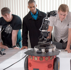 Three computer science students leaning on table and looking at robot