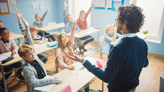 Students sitting at desks and raising hands while teacher stands with his arms extended