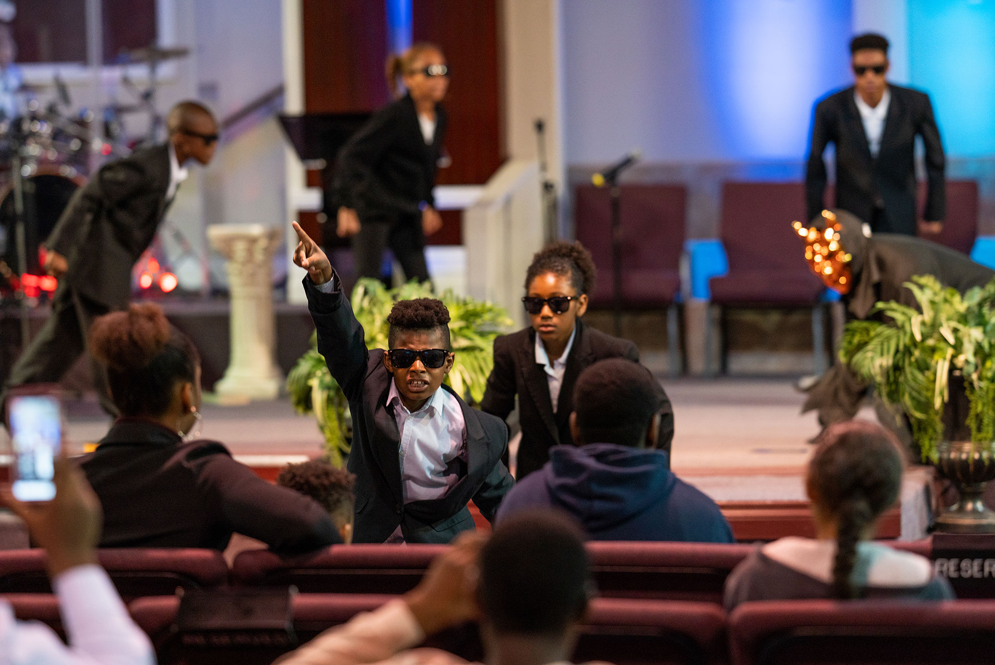 Young boy in suit and sunglasses pointing at the ceiling