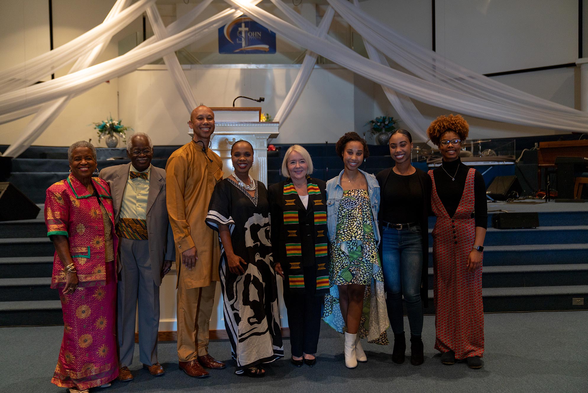 Eight people standing shoulder to shoulder and smiling