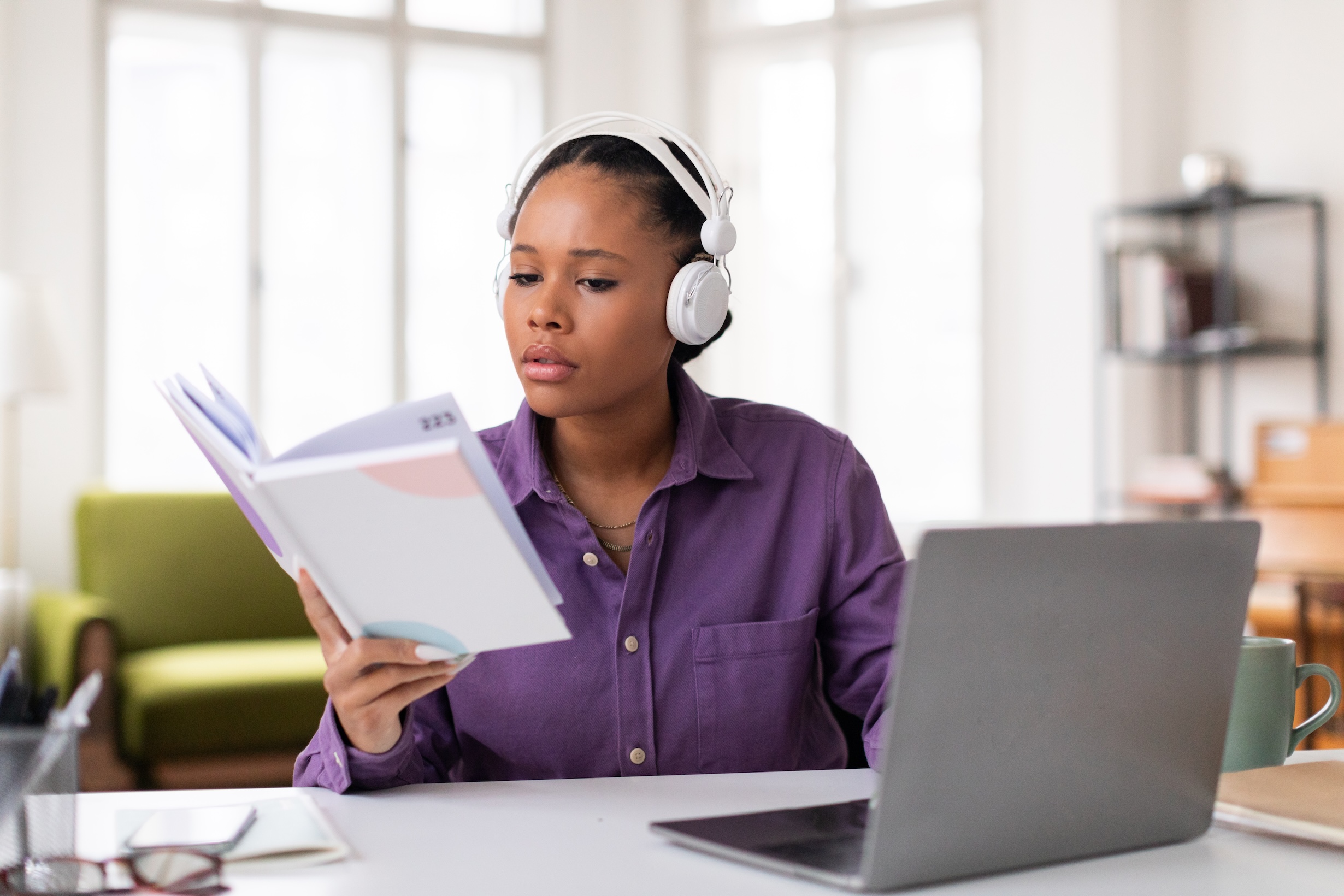 a professor looks at a notebook with headphones on in front of a laptop