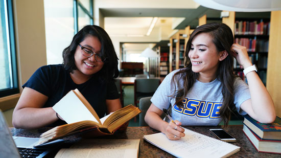 Two female students reading books in a library