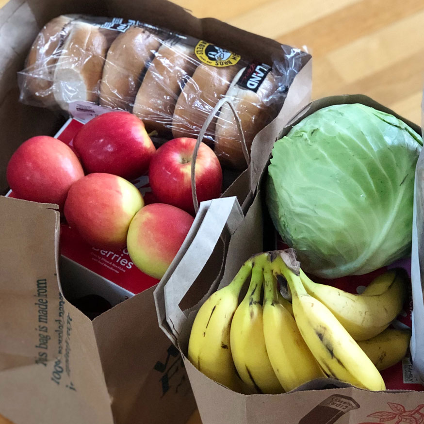 Two brown paper bags filled with apples, bananas, and other groceries