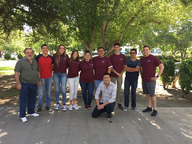 A group of students and a mentor stand together outdoors under trees during a summer research program