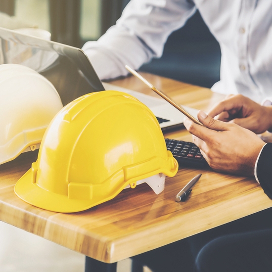 Yellow hard hat next to a laptop on a wooden desk