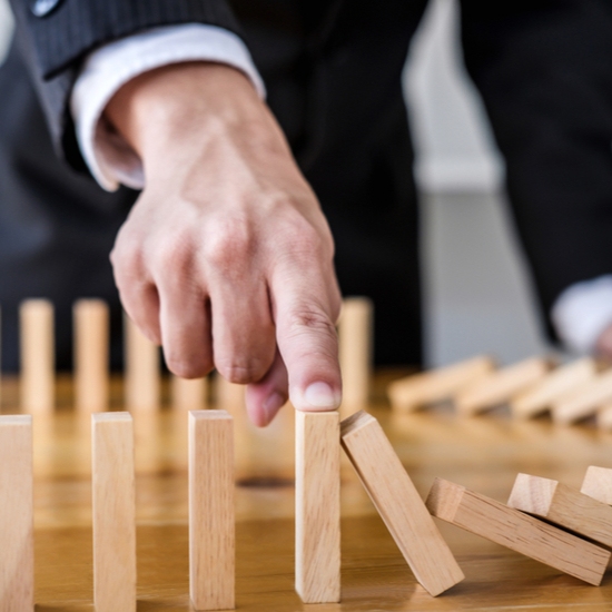 Businessman hand stopping wooden dominoes from falling