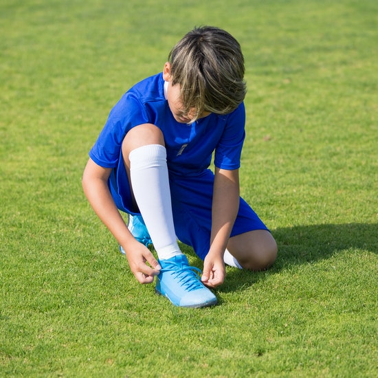 Young boy in blue soccer uniform kneeling on grass and looking at his right foot