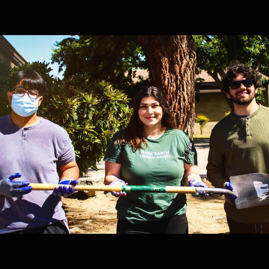 Three students holding a shovel