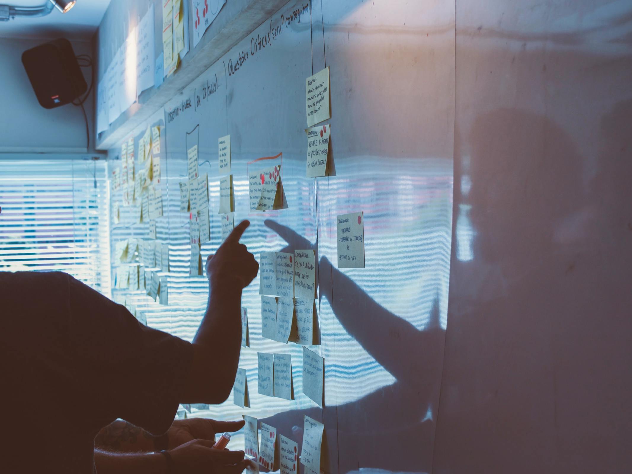 Silhouette of arm pointing to a whiteboard covered in sticky notes